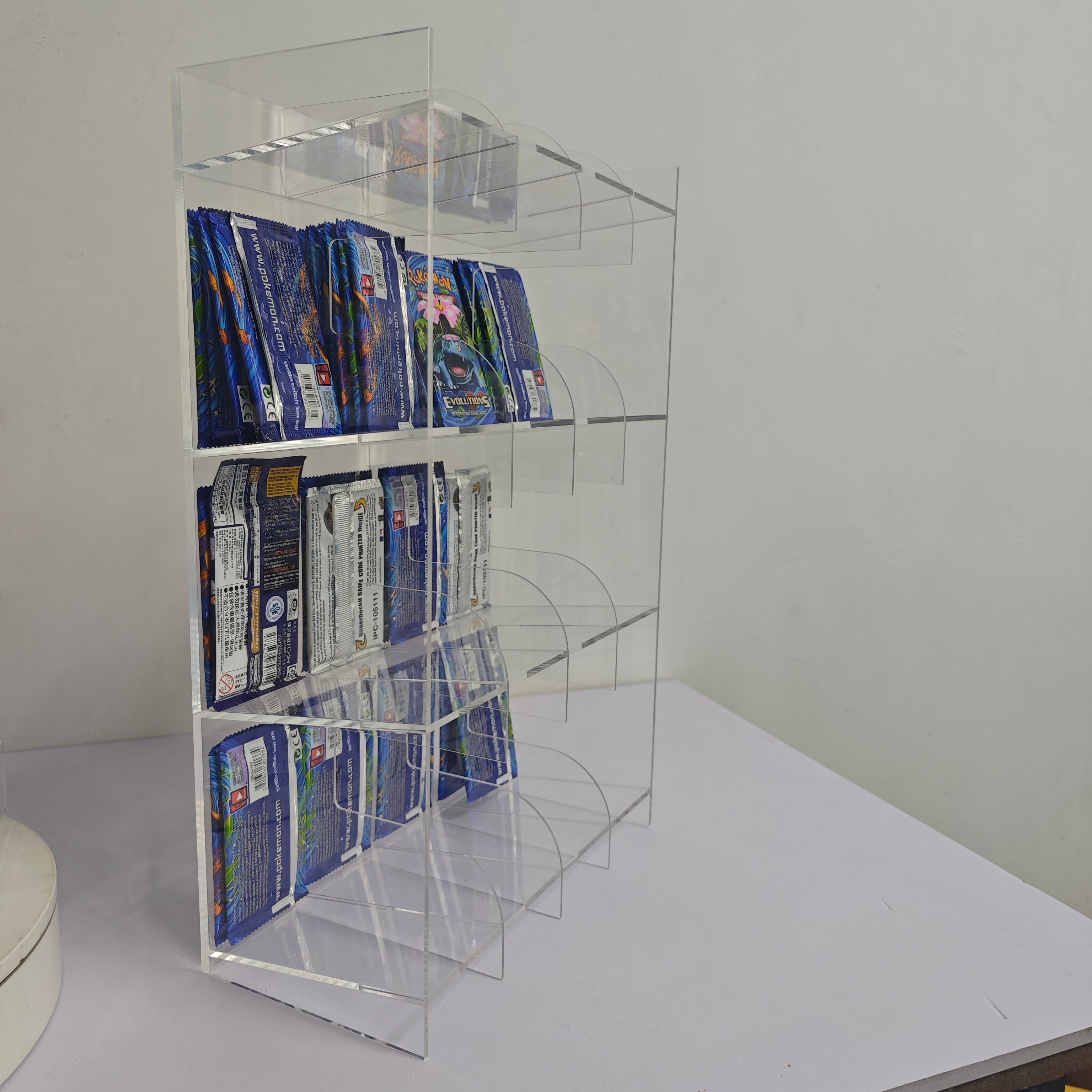 Side view of a clear acrylic display stand holding a variety of trading card booster packs.