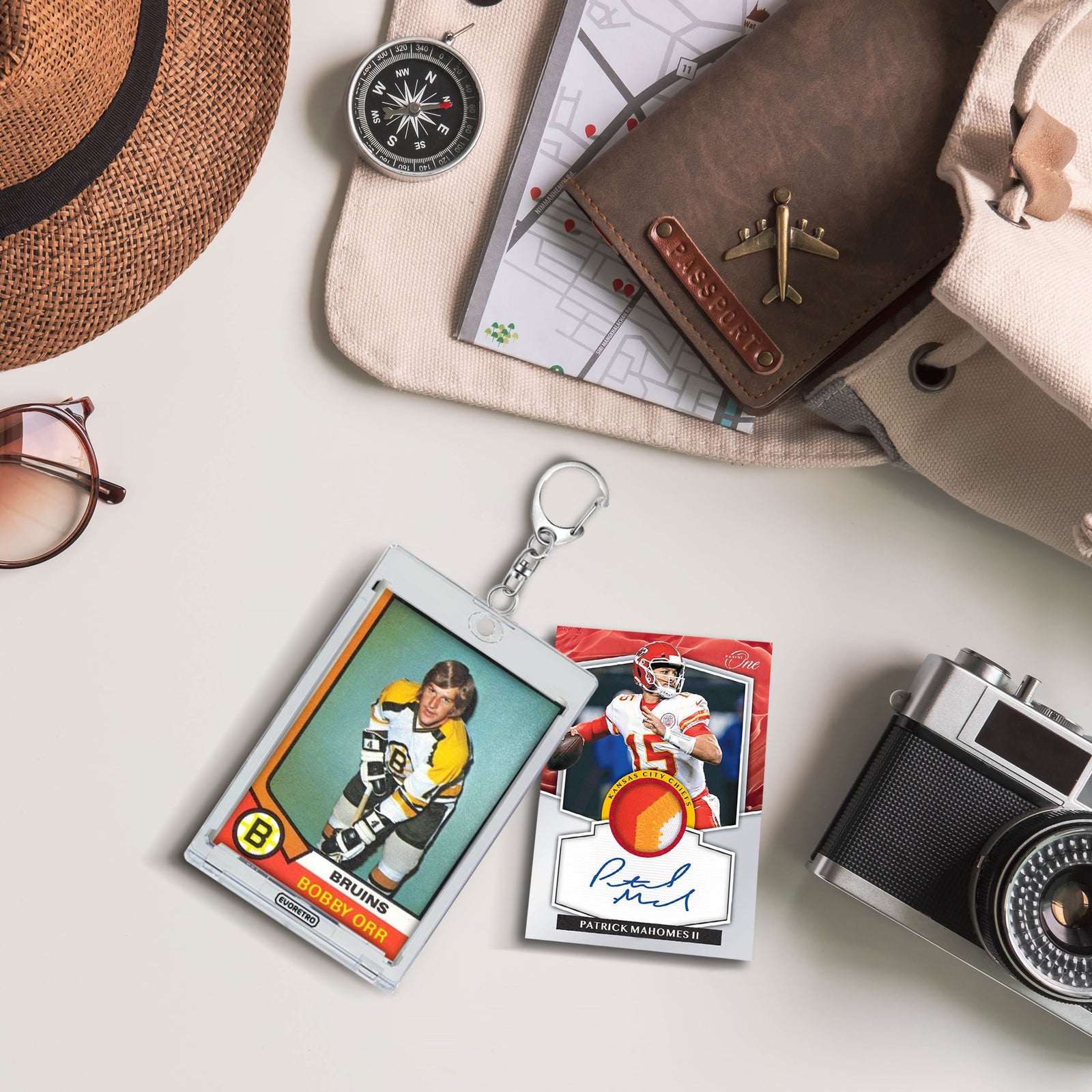 Sports card displayed in magnetic TCG keychain holder, with another card, camera, hat, and map on light surface.