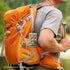 Person wearing an orange backpack with a card holder attached, outdoors.