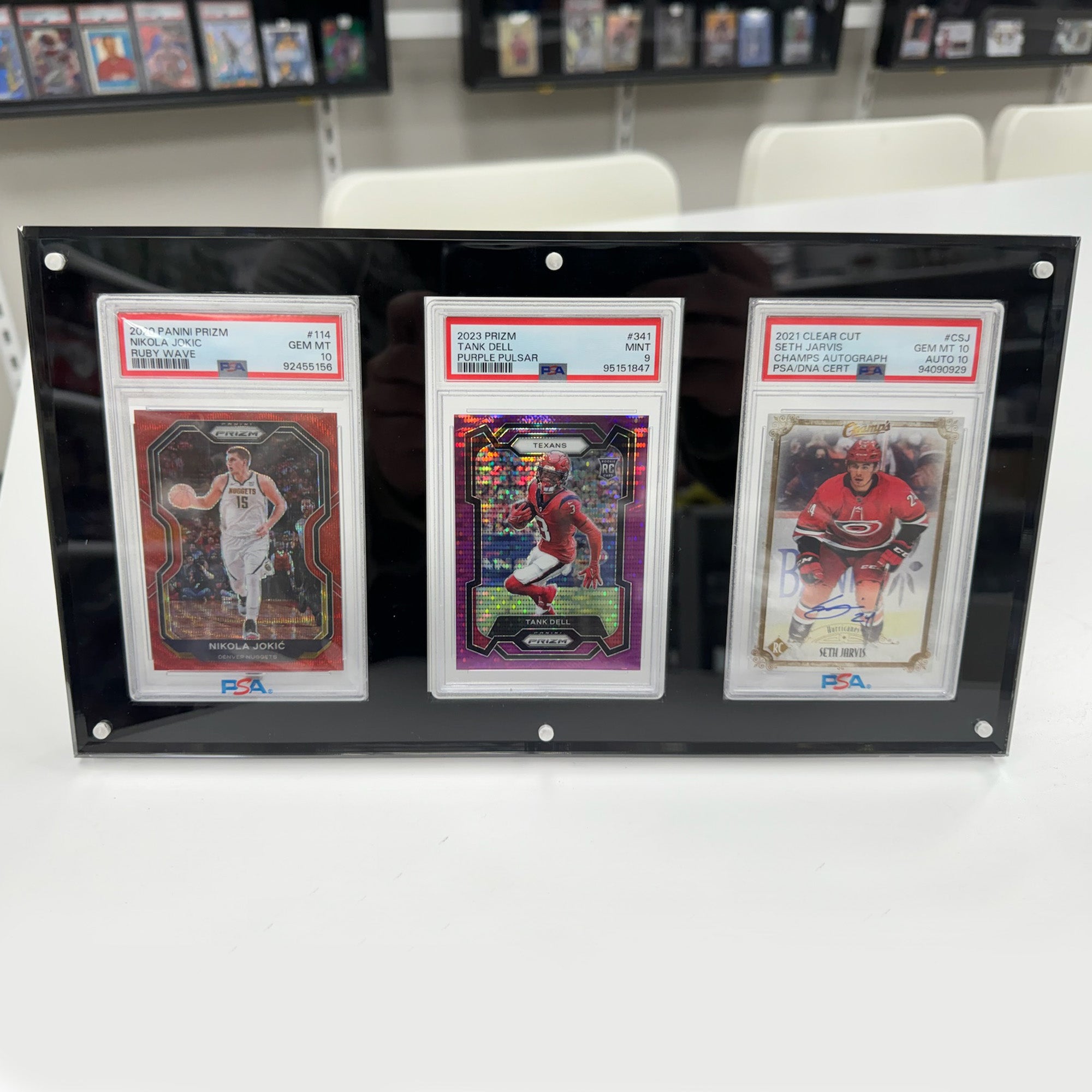 Three sports trading cards in a display case on a white surface with a store shelf in the background.